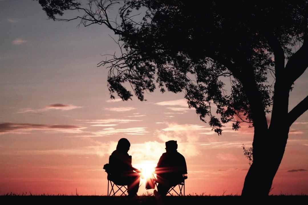 two silhouettes sitting in front of a tree at sunset